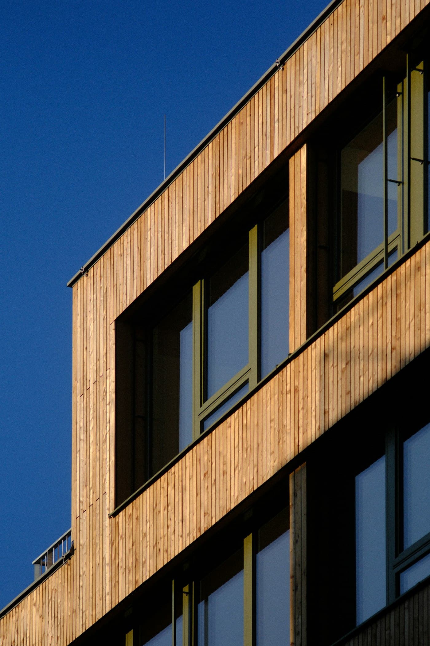 A timber-clad facade with deep-set dark window frames against a blue sky