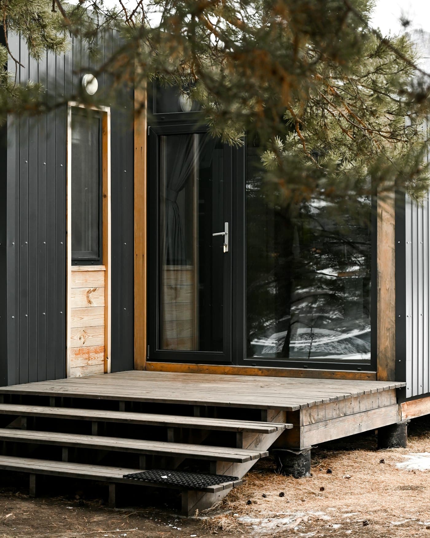A dark-clad cabin with a glazed door and timber steps up to a small deck