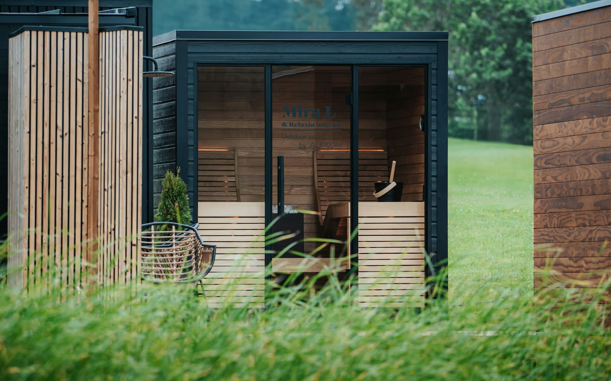 A dark-clad garden room with a timber-lined recessed front, standing in long grass