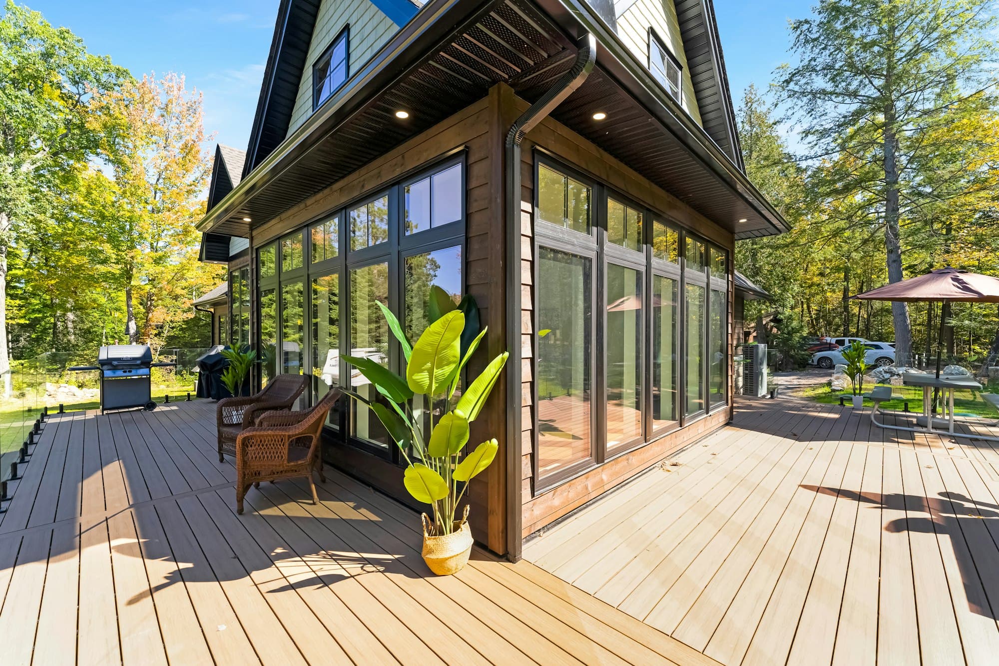 A timber deck wrapping around a glazed room, with wicker seating