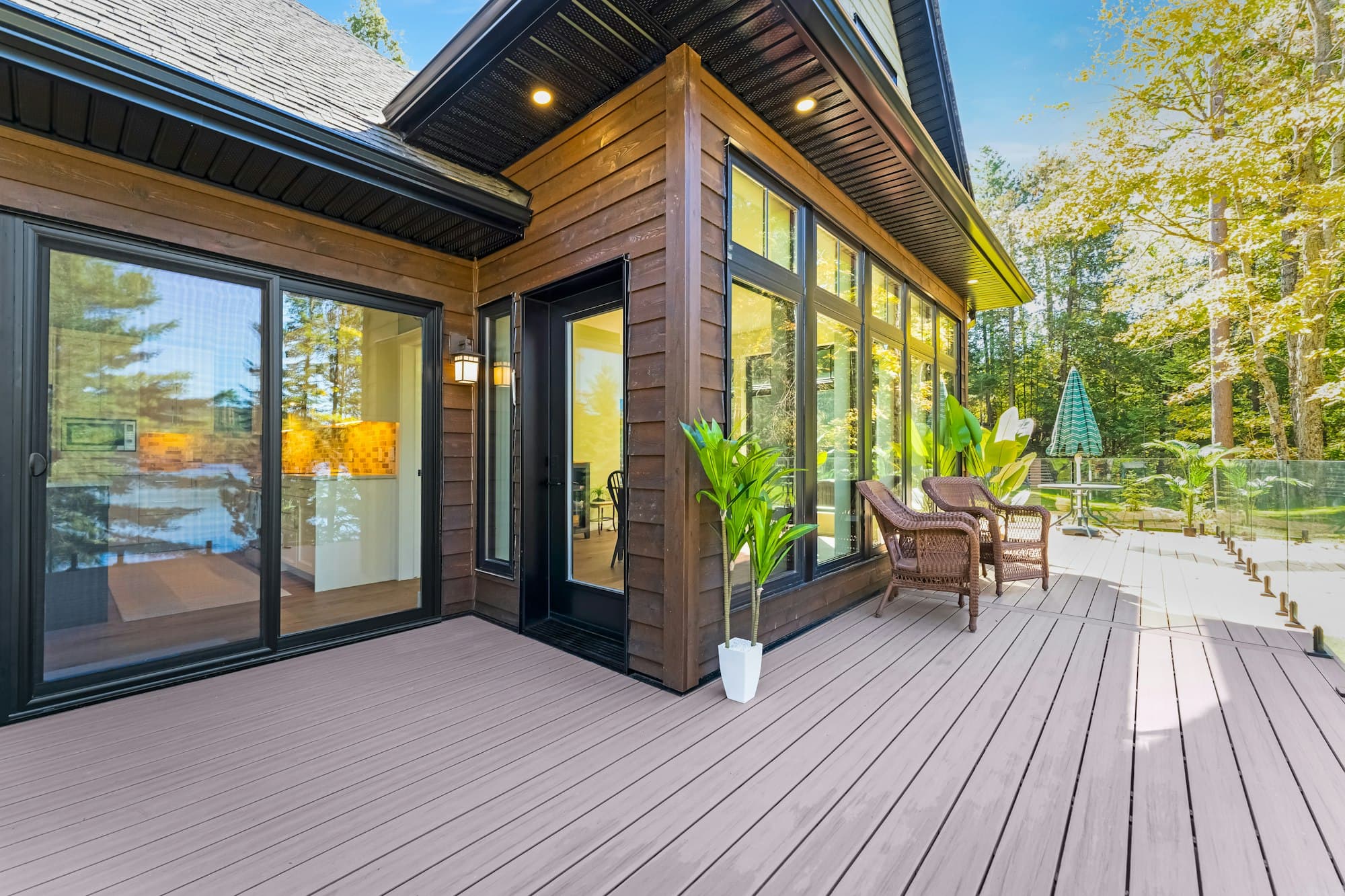 A glazed room opening onto a timber deck with wicker chairs and a potted plant