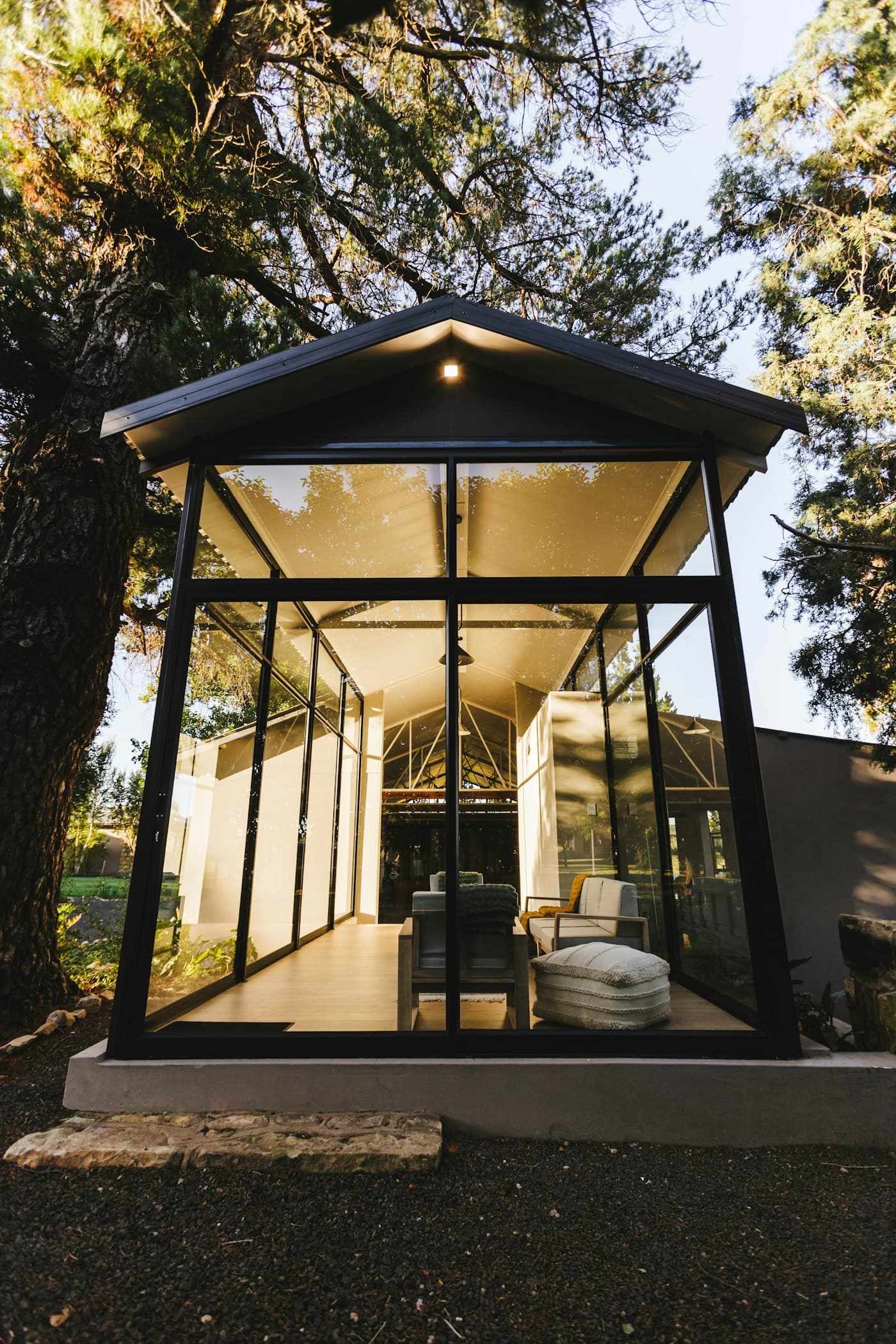 A glass-fronted gabled garden building lit from within at dusk