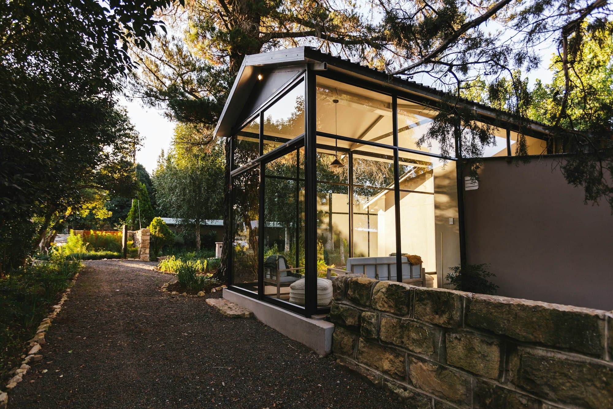 A glazed garden pavilion with a slim dark frame beside a stone wall