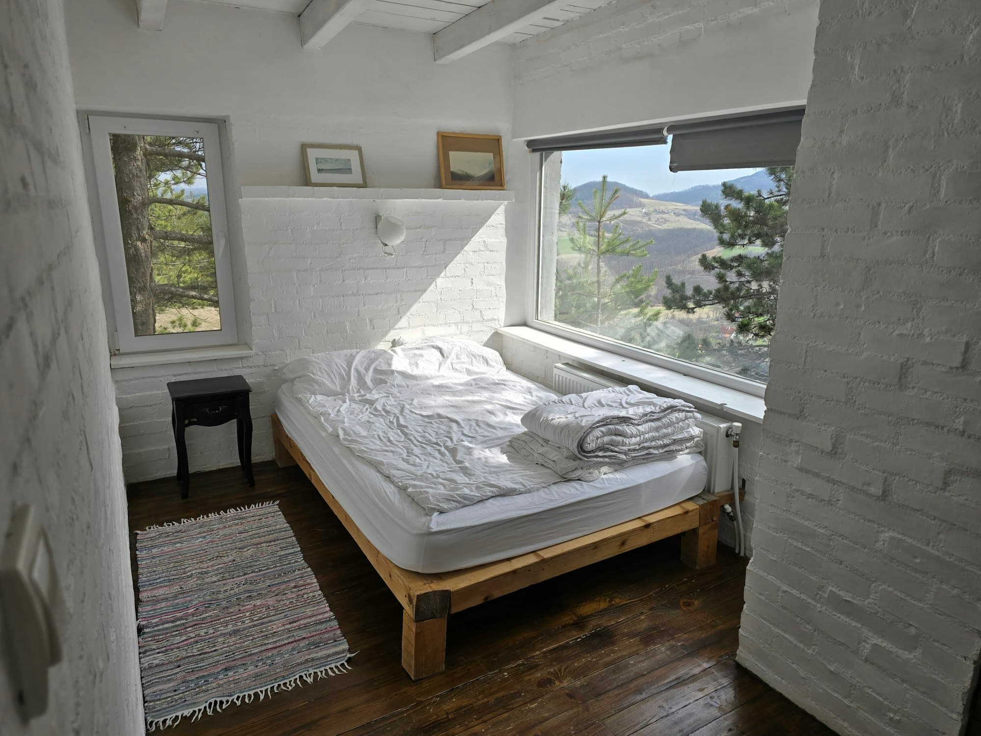 A simple bedroom with a low bed and a large window onto hills
