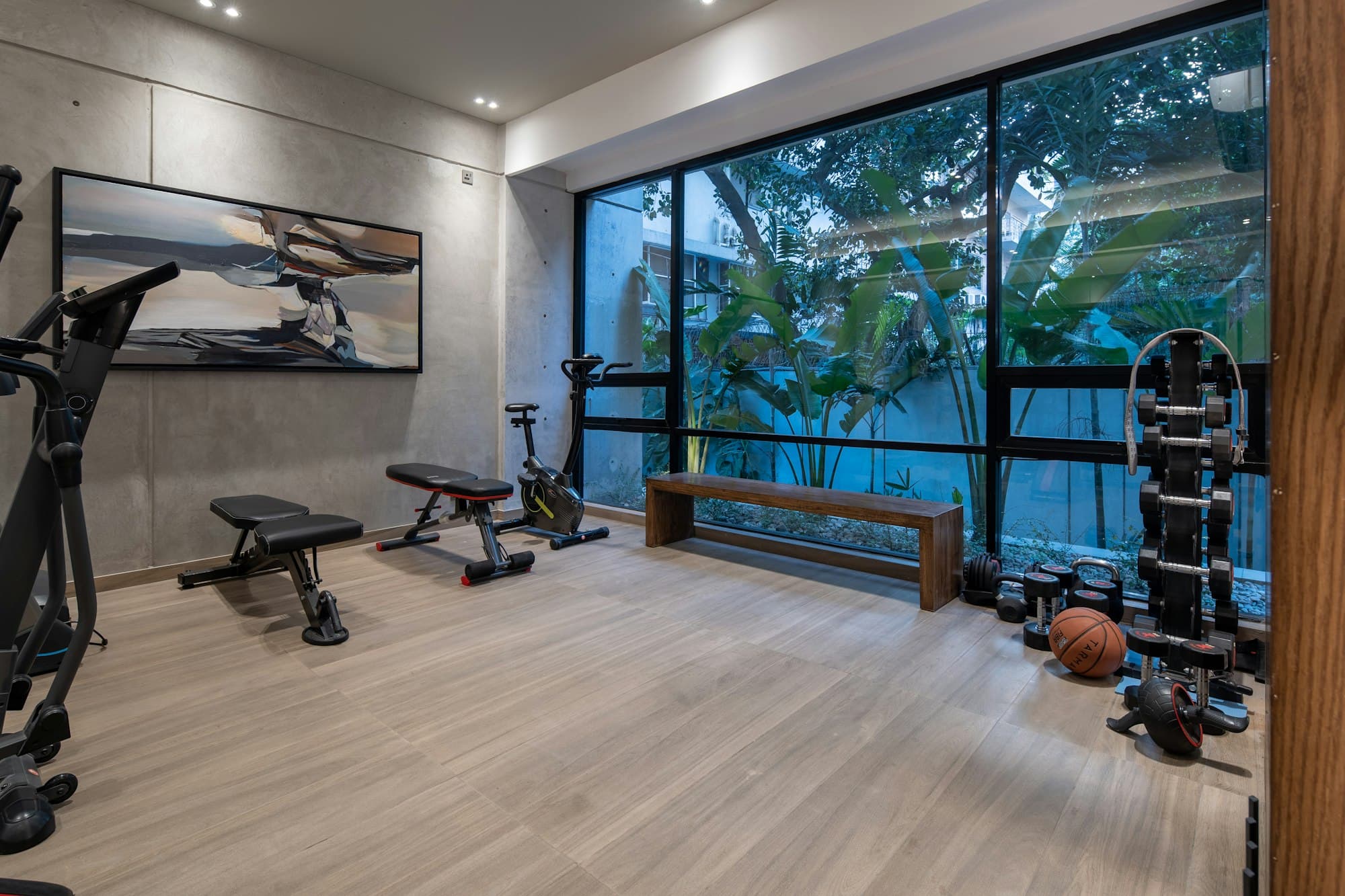 A home gym with a bench and equipment in front of full-height glazing and greenery
