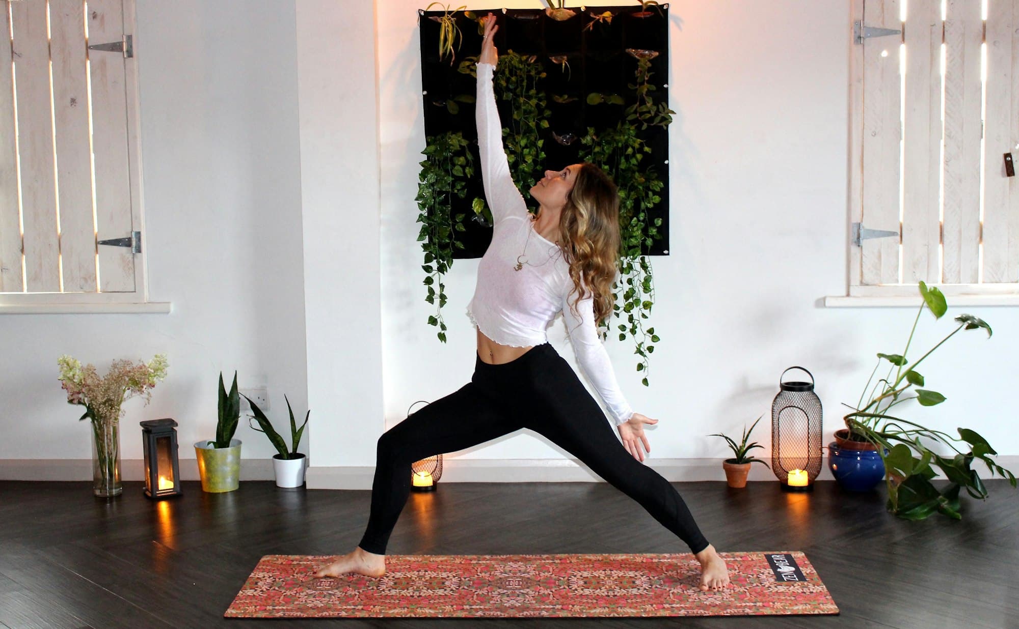A woman holding a yoga pose on a rug, trailing plants on the wall behind