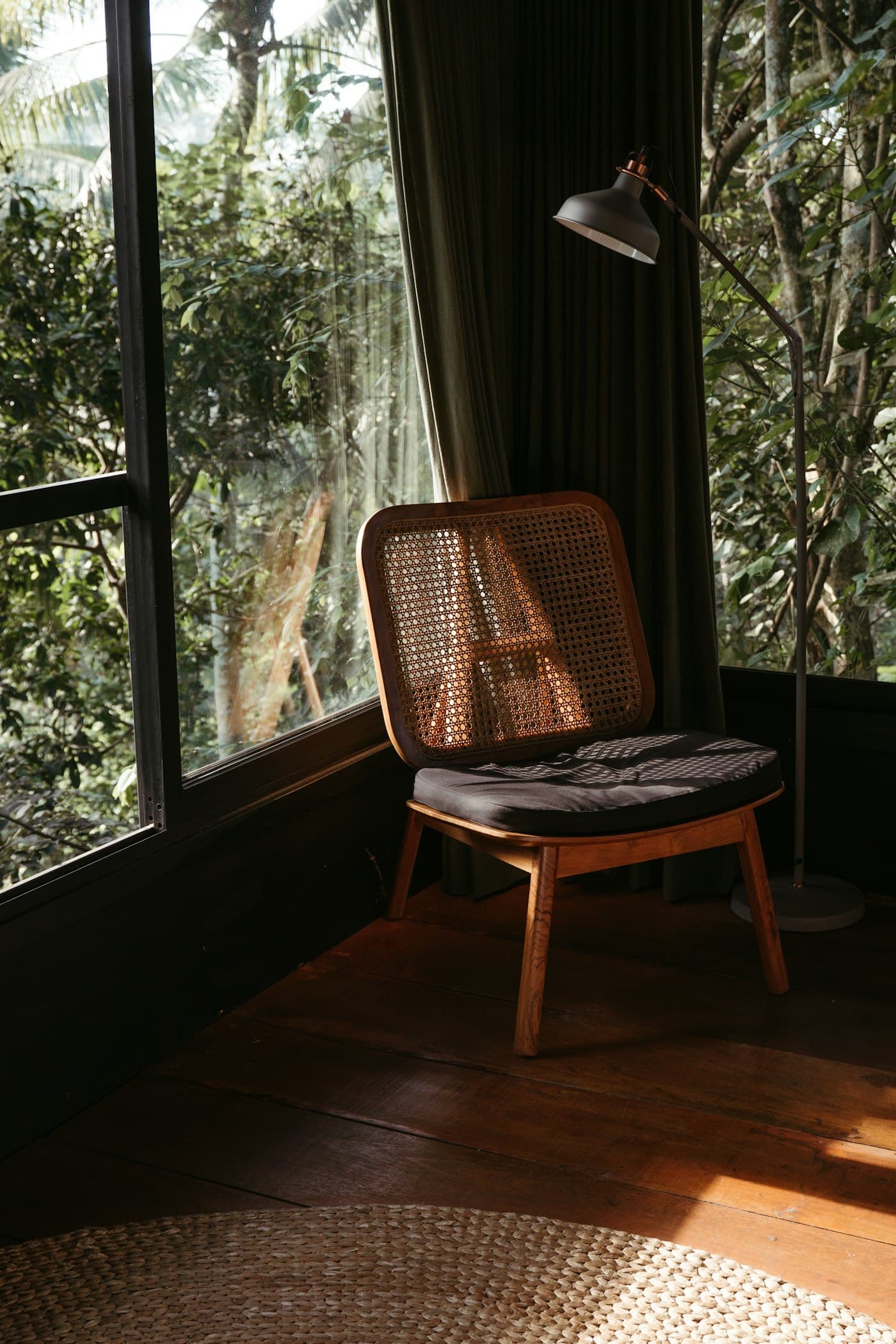 A cane-backed armchair beside dark-framed windows looking onto leaves