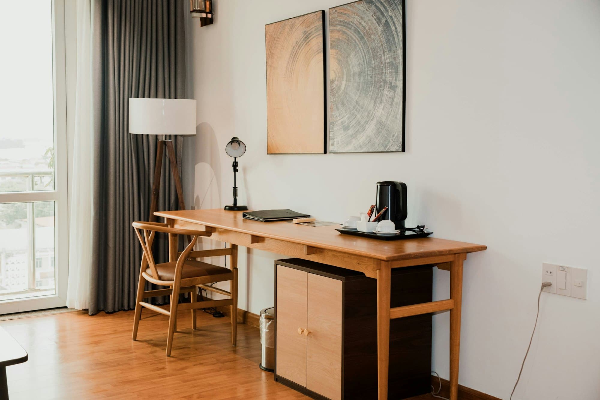 A warm wooden desk with a chair and lamp beneath framed artwork