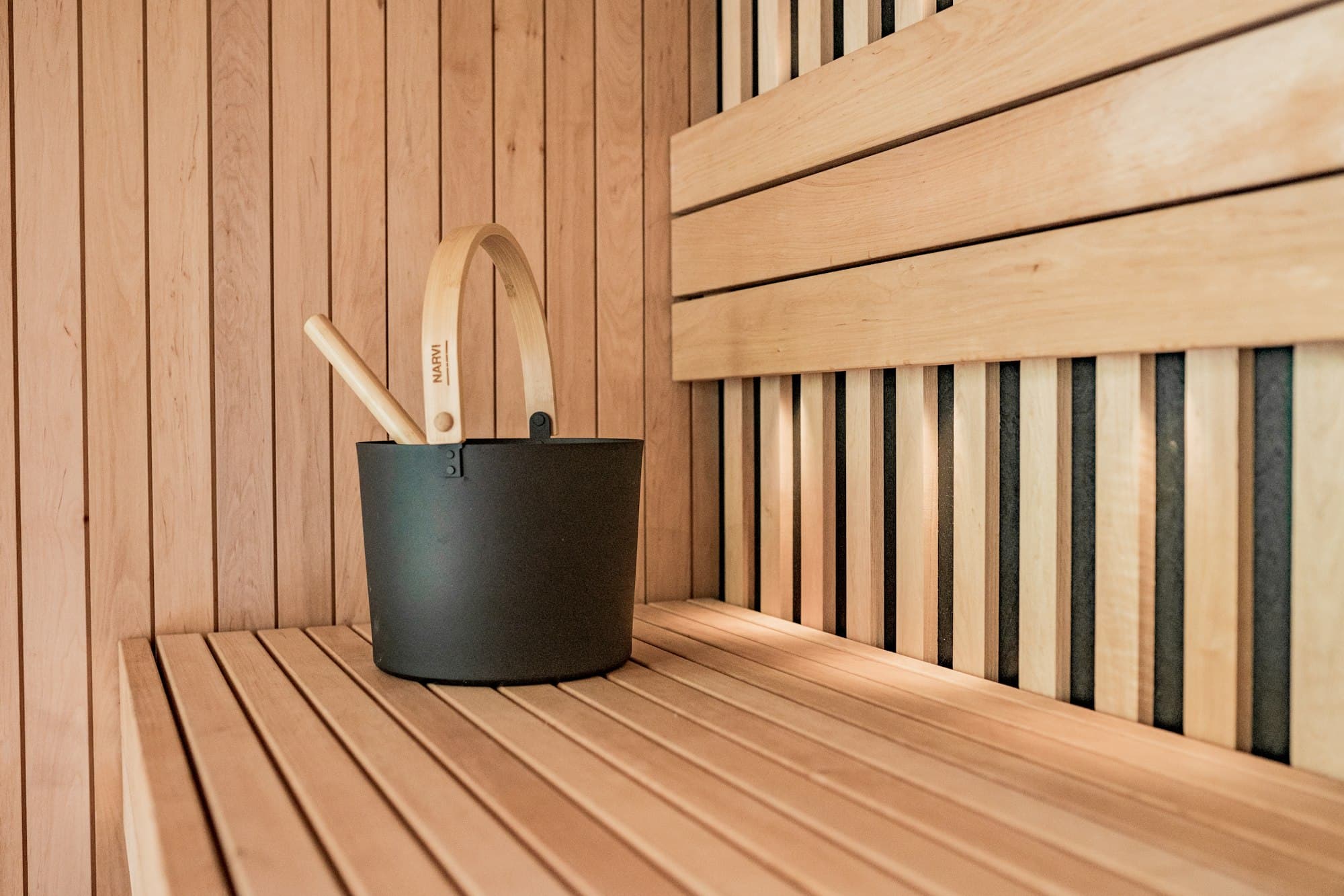 A sauna bucket and ladle on a pale timber bench