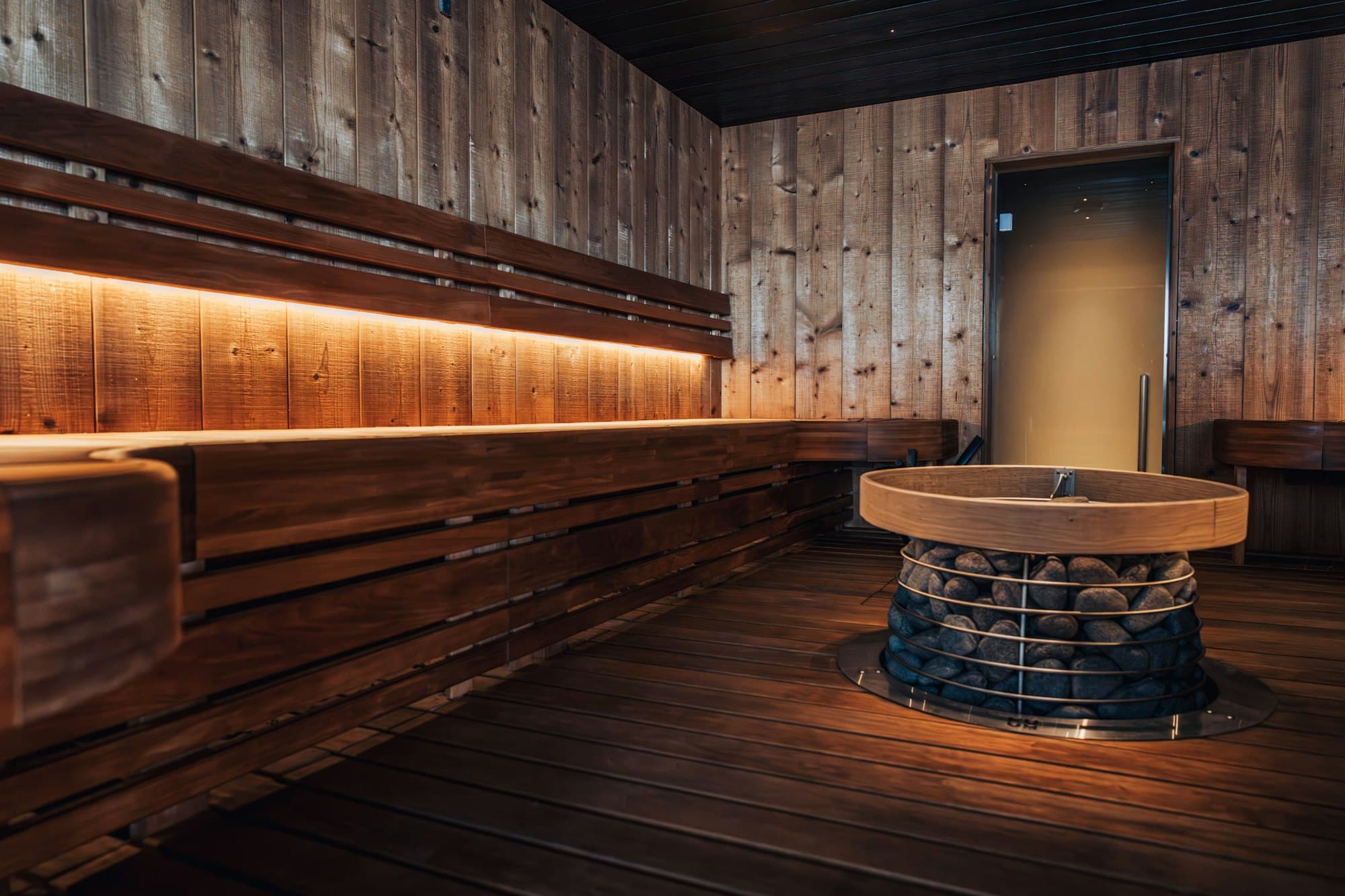 A dark timber sauna with tiered benches and a heater
