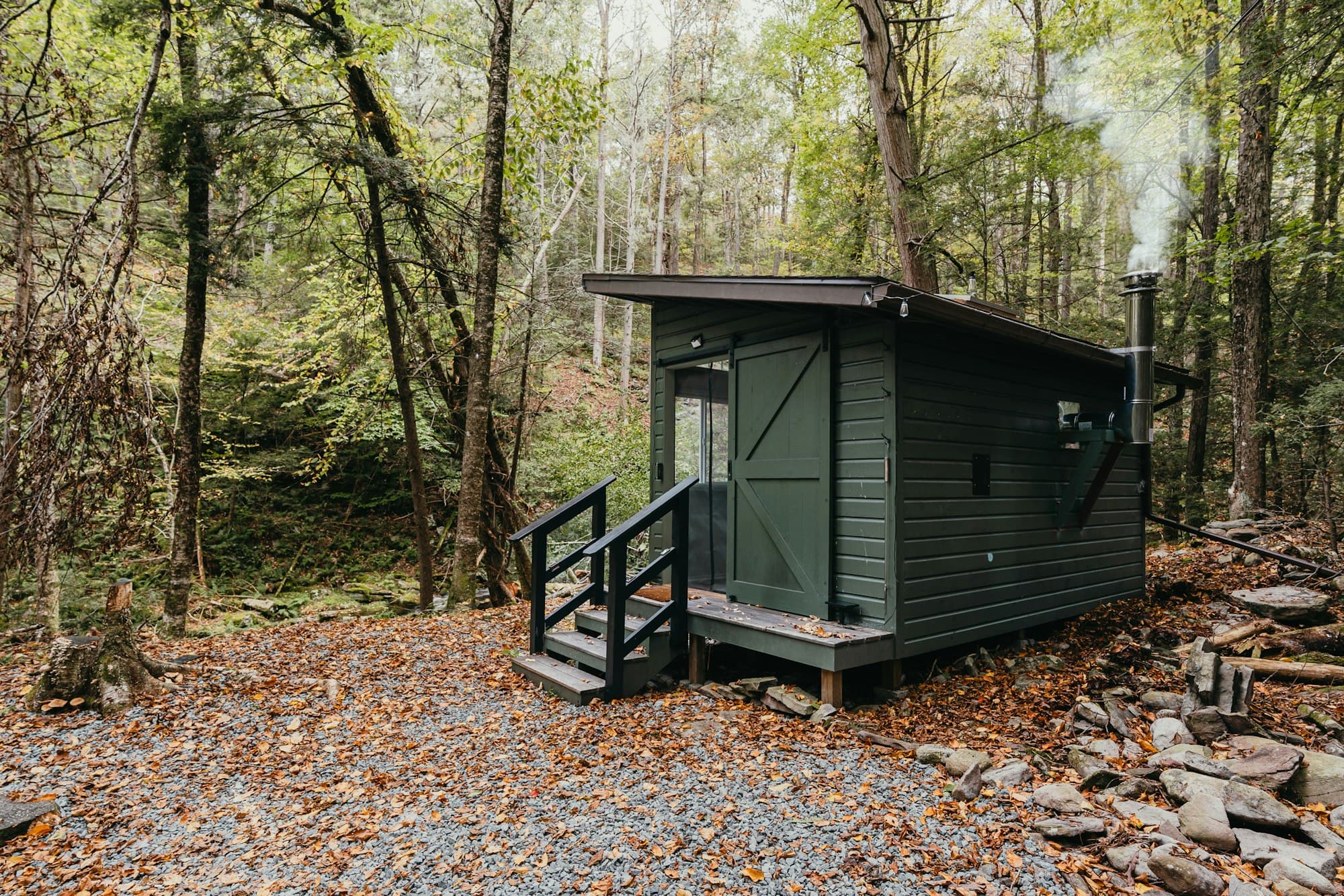 A small dark green garden building with steps up to its door, set among trees