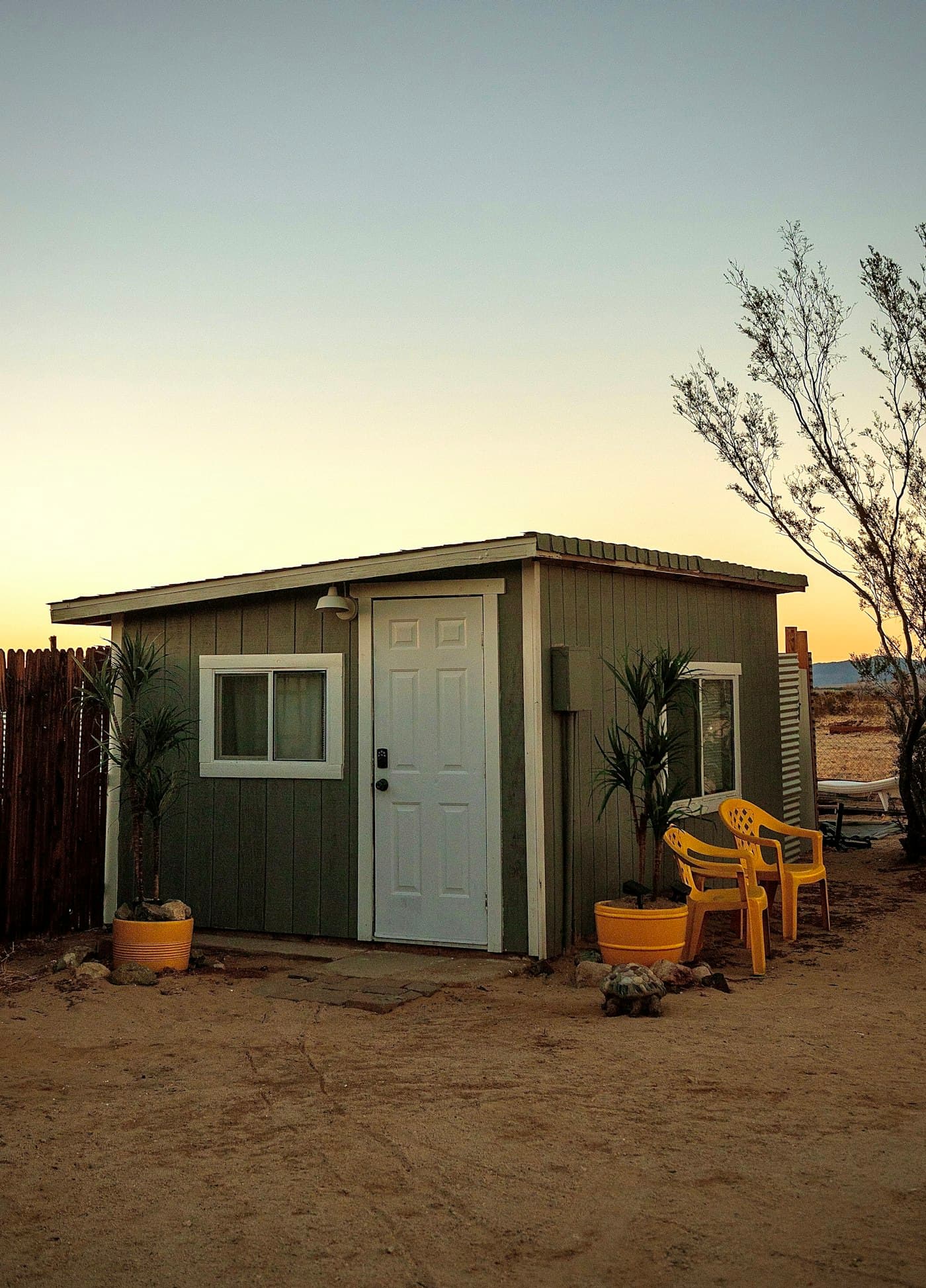 A compact garden room with a pale door and two yellow chairs outside at dusk