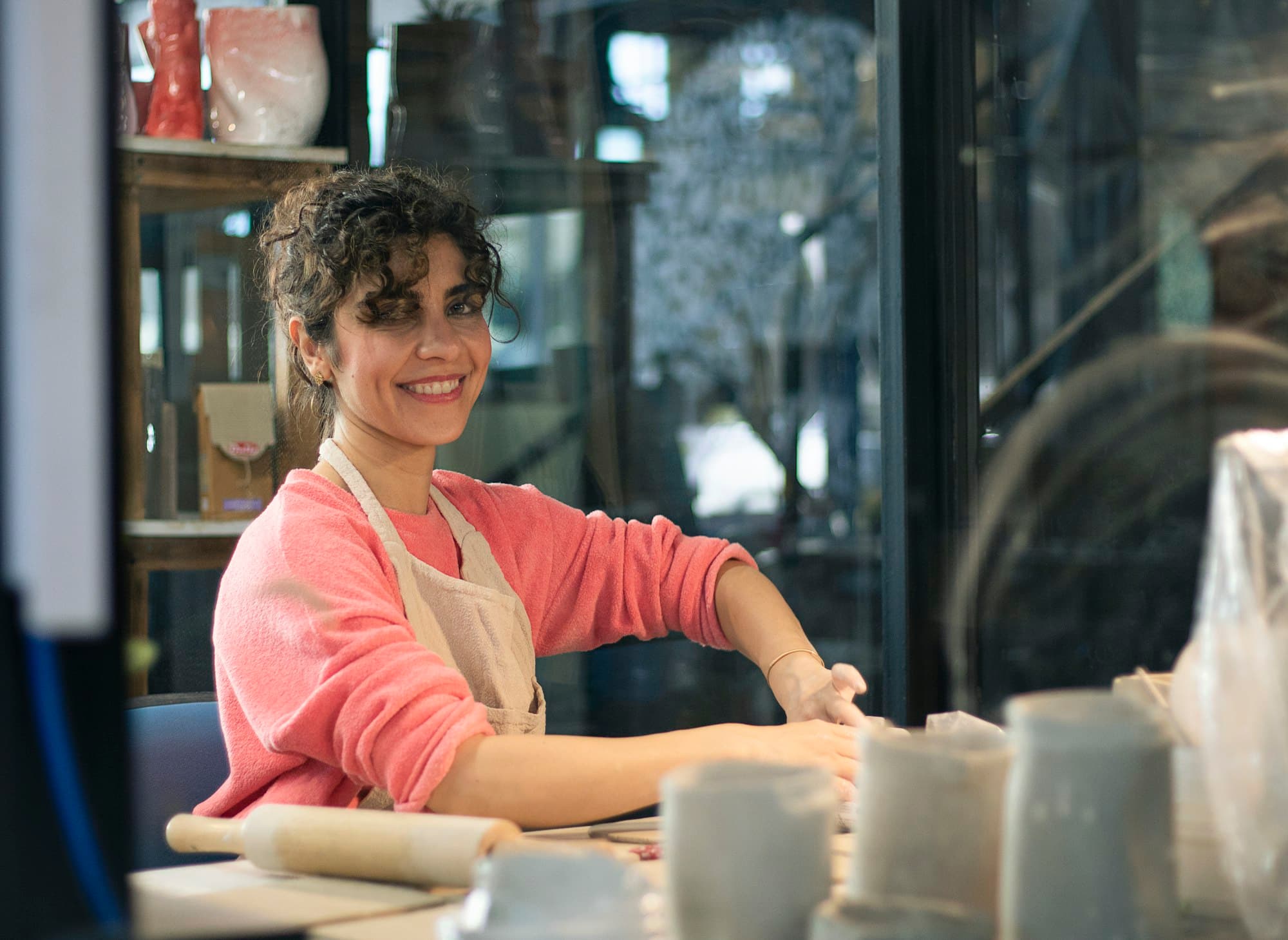 A ceramicist smiling at her workbench in front of a window